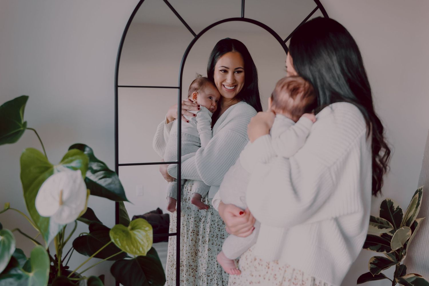 Two people share a tender moment with infants in a bright interior setting with houseplants.
