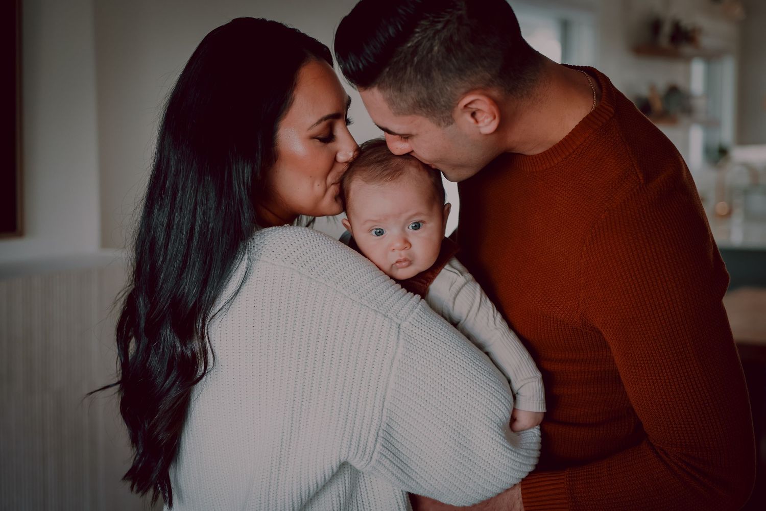 An intimate family moment with a small baby being embraced by adults in warm sweaters.