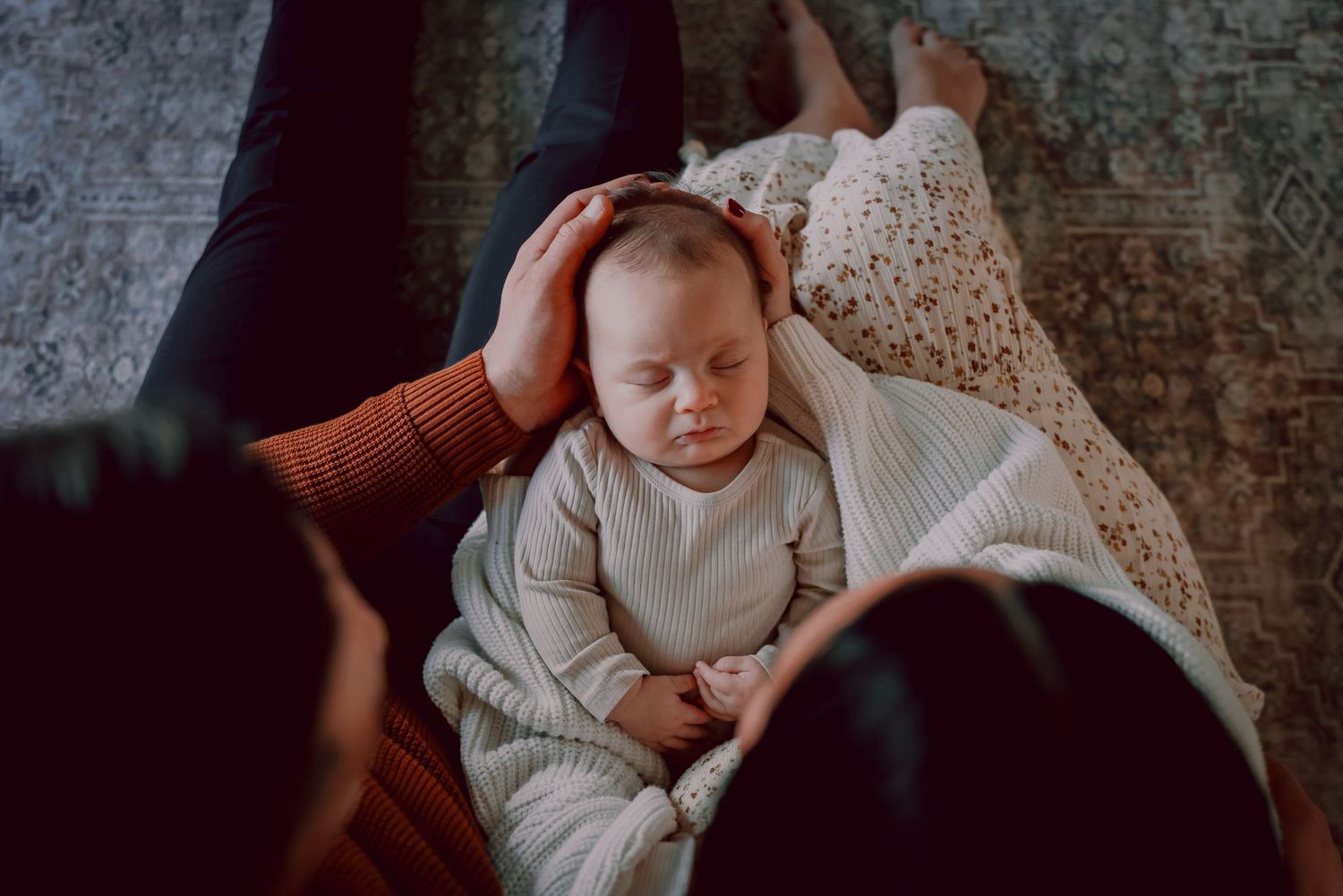 A sleeping infant in white clothing rests peacefully while being gently touched.