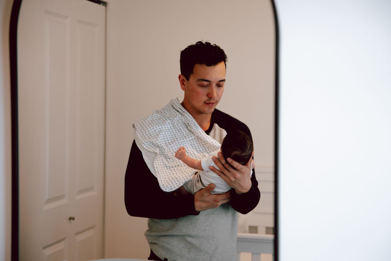 Person in dark clothing holding and looking down at a swaddled newborn.