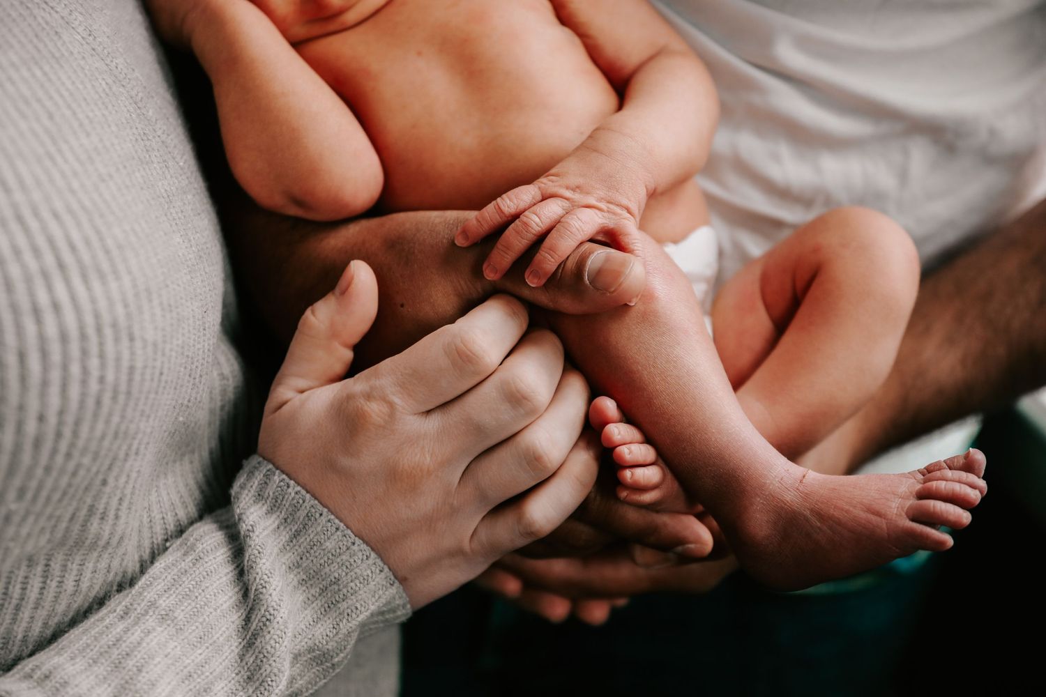 Gentle hands hold a baby's tiny feet against soft fabric.