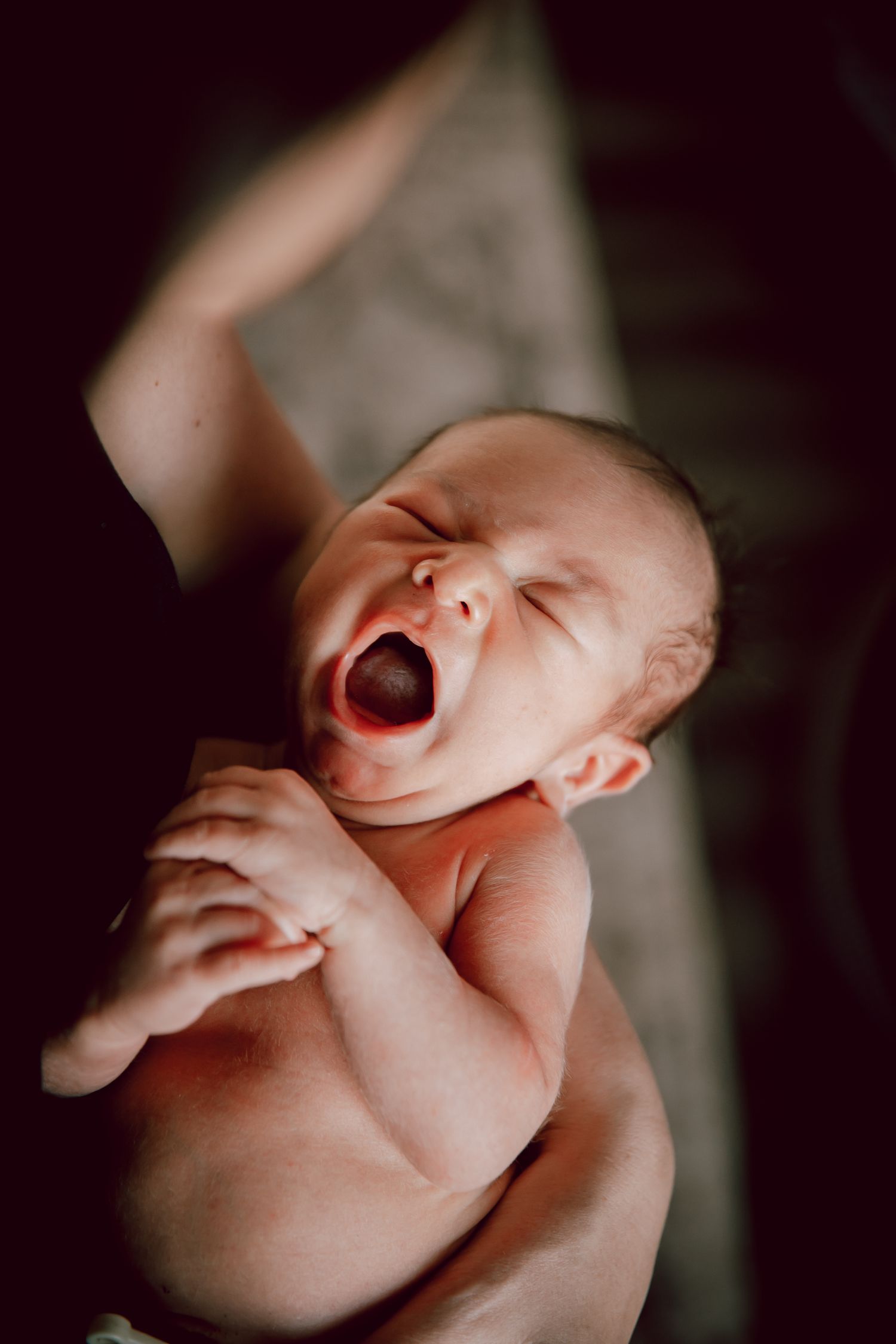 Close-up portrait of a yawning naked newborn baby in dramatic lighting.