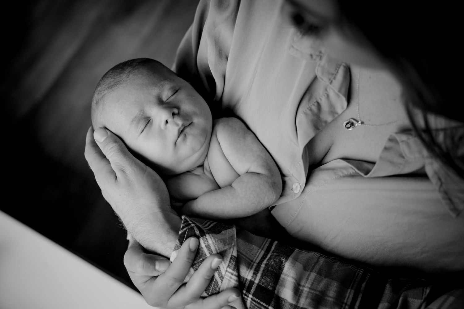 Peaceful black and white image of a newborn baby resting on a caregiver's chest.