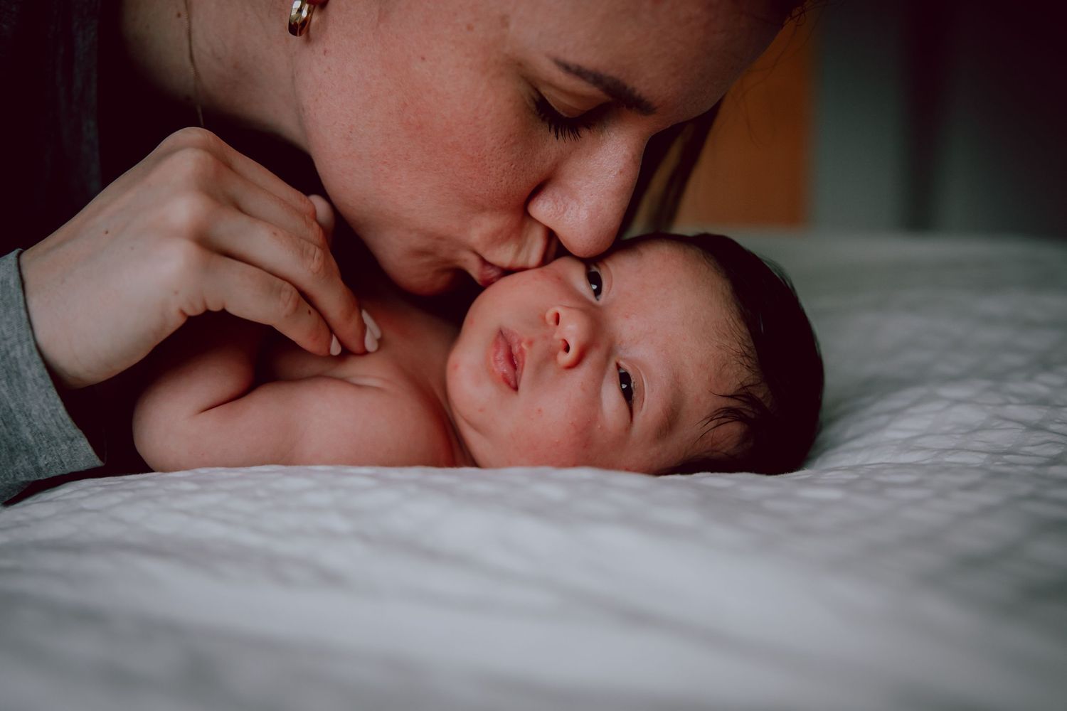 Intimate close-up of a tender moment between caregiver and sleeping infant on white bedding.
