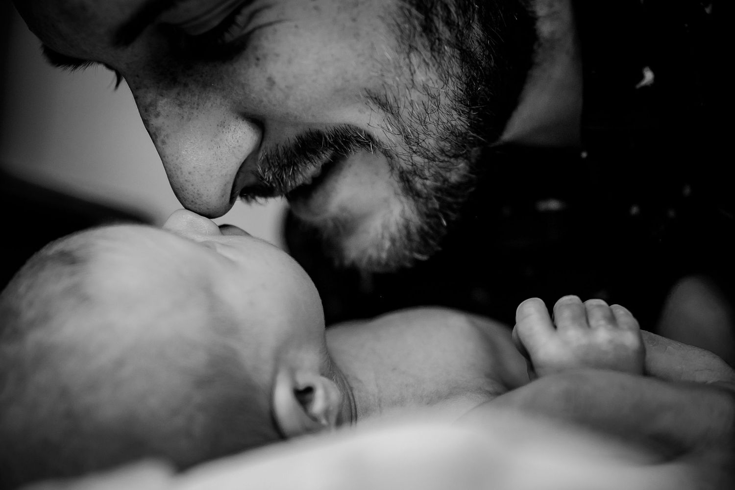 A tender black and white close-up moment between a parent and infant.