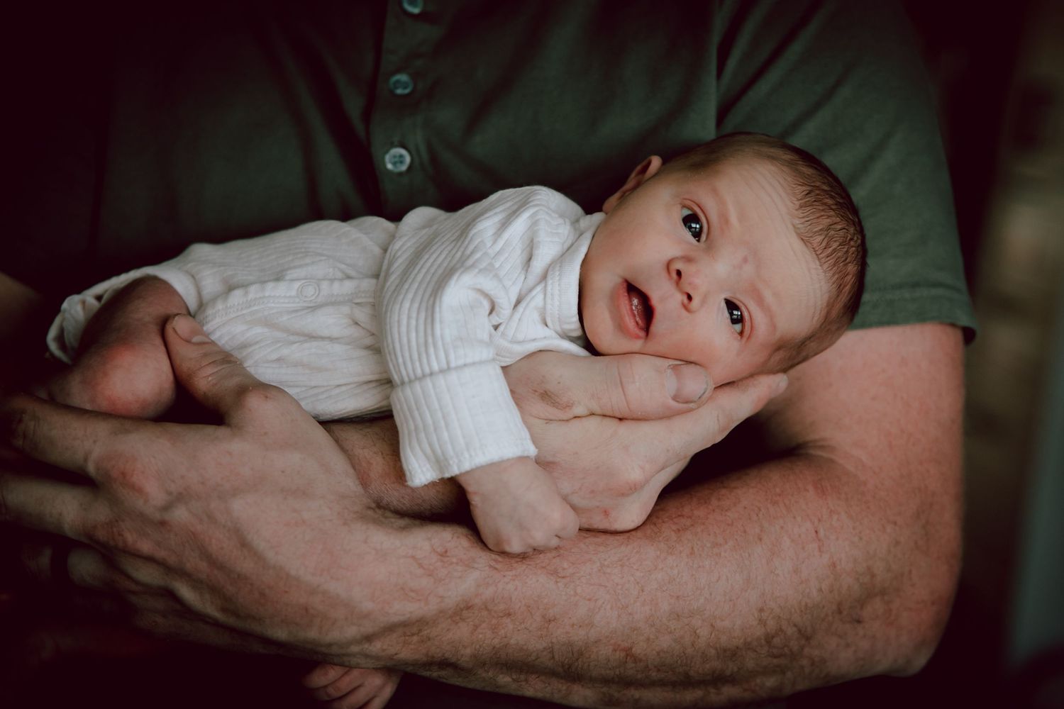 Baby in white onesie rests on parent's forearm.