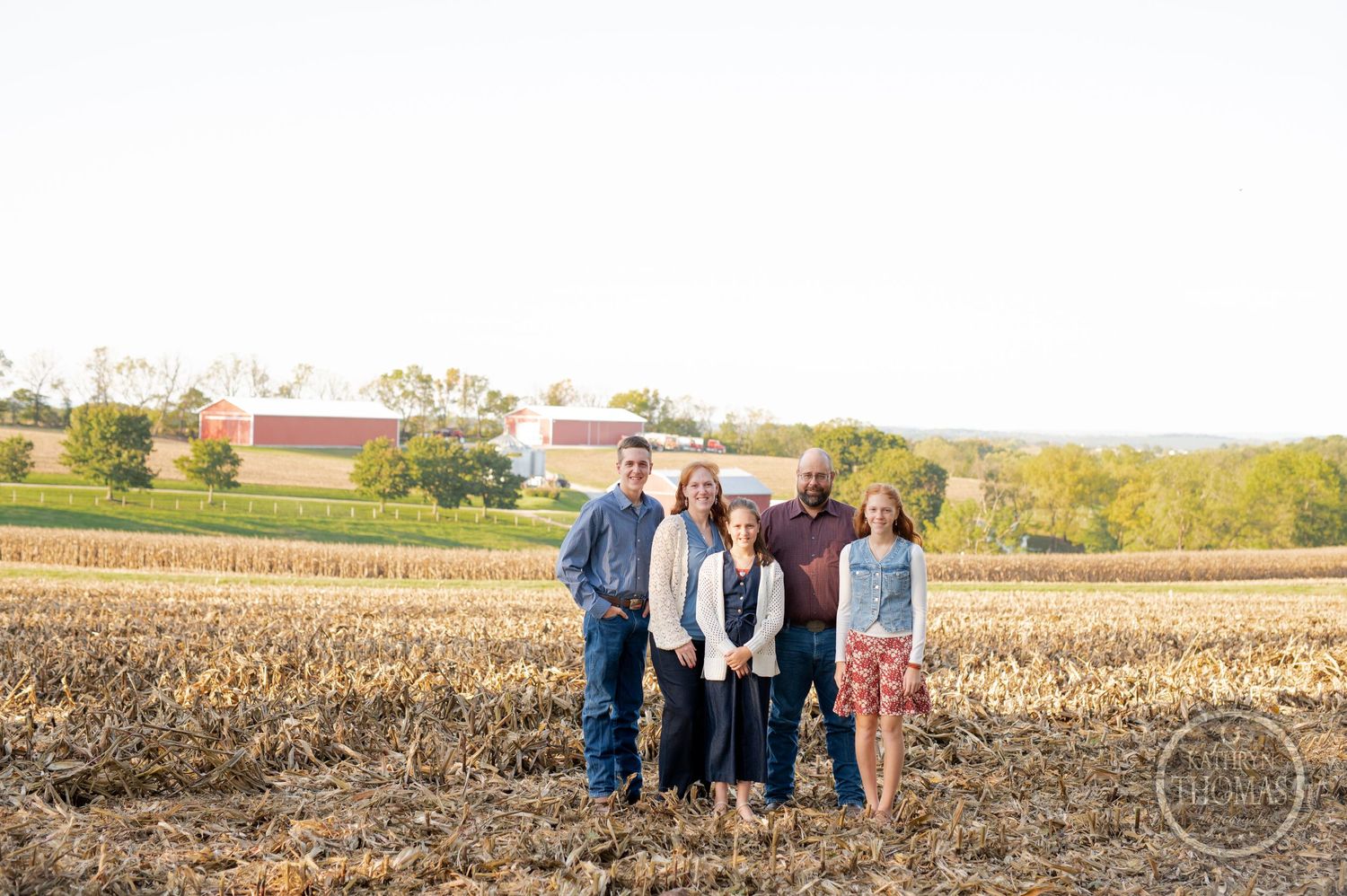 Family group photo in a harvested cornfield with farm buildings in background.