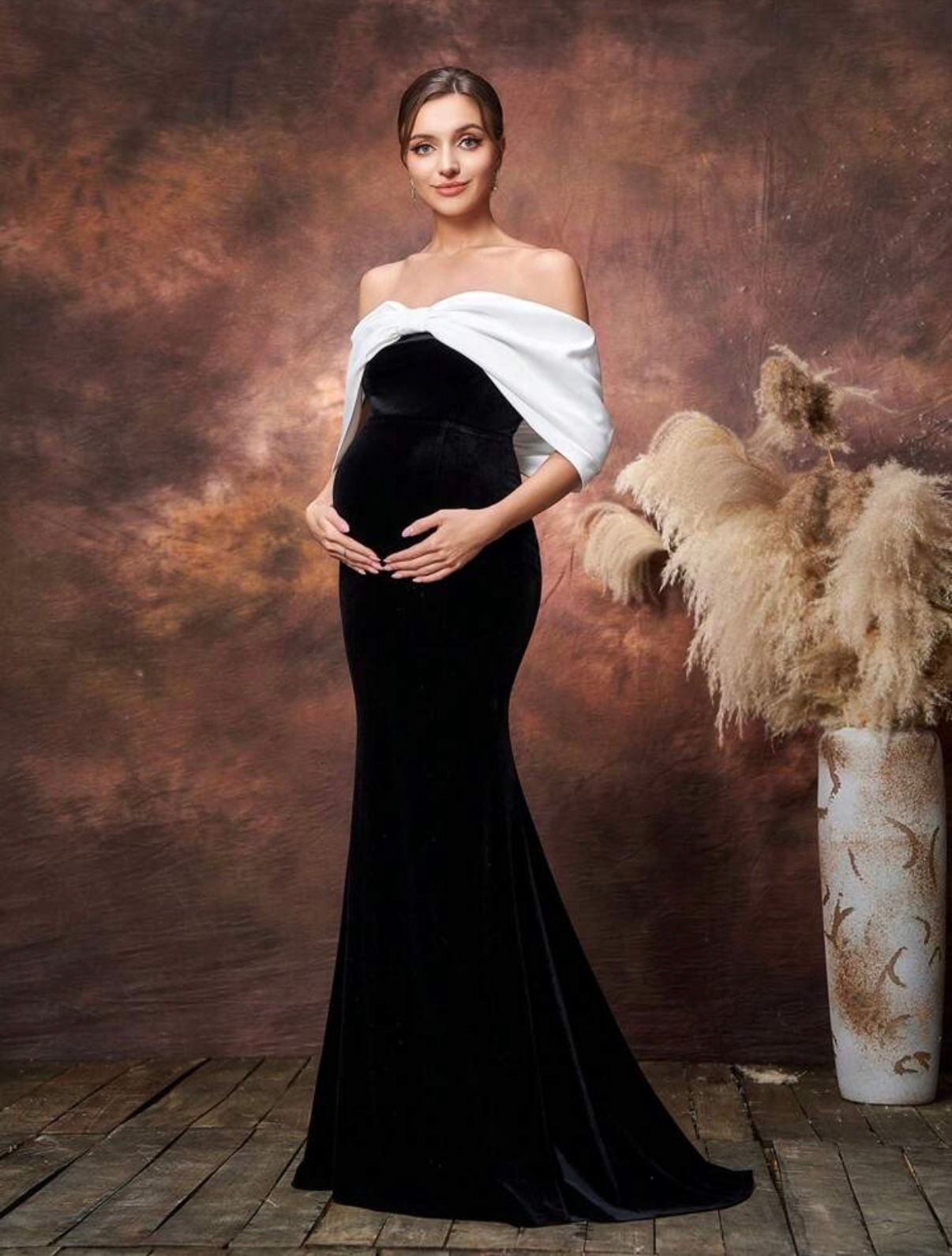 Elegant maternity photos with flowing black dress against dark brown backdrop with pampas grass decor.