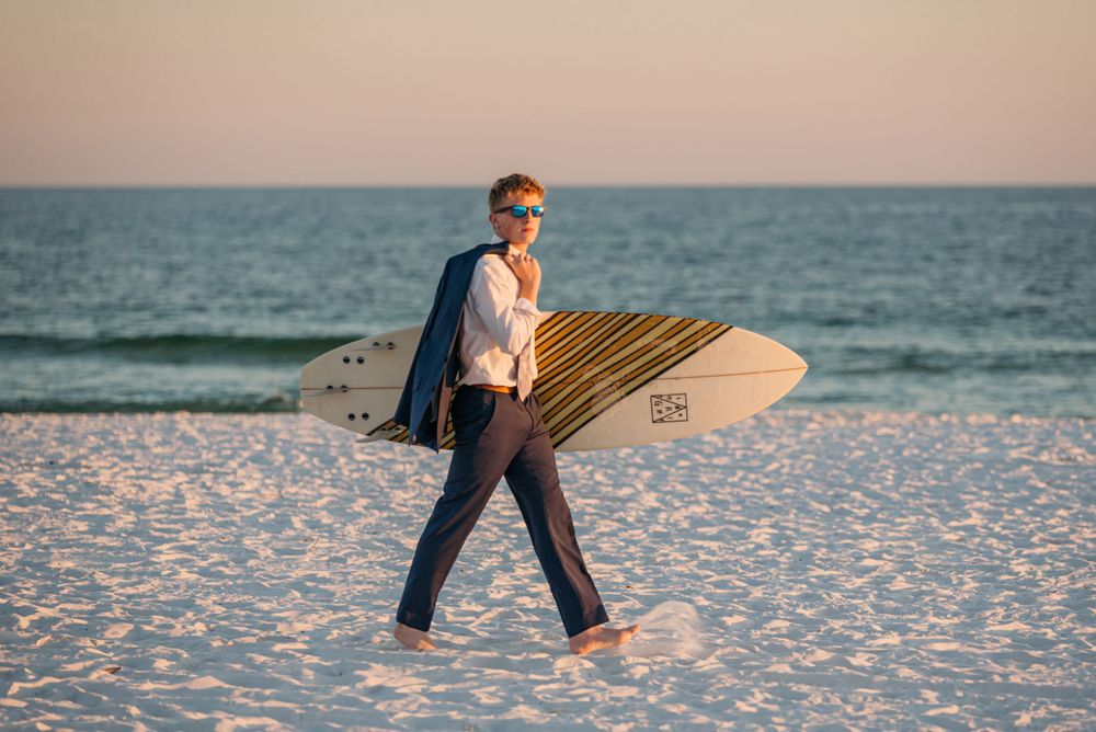 People walking with surfboards on white sand beach during sunset.
