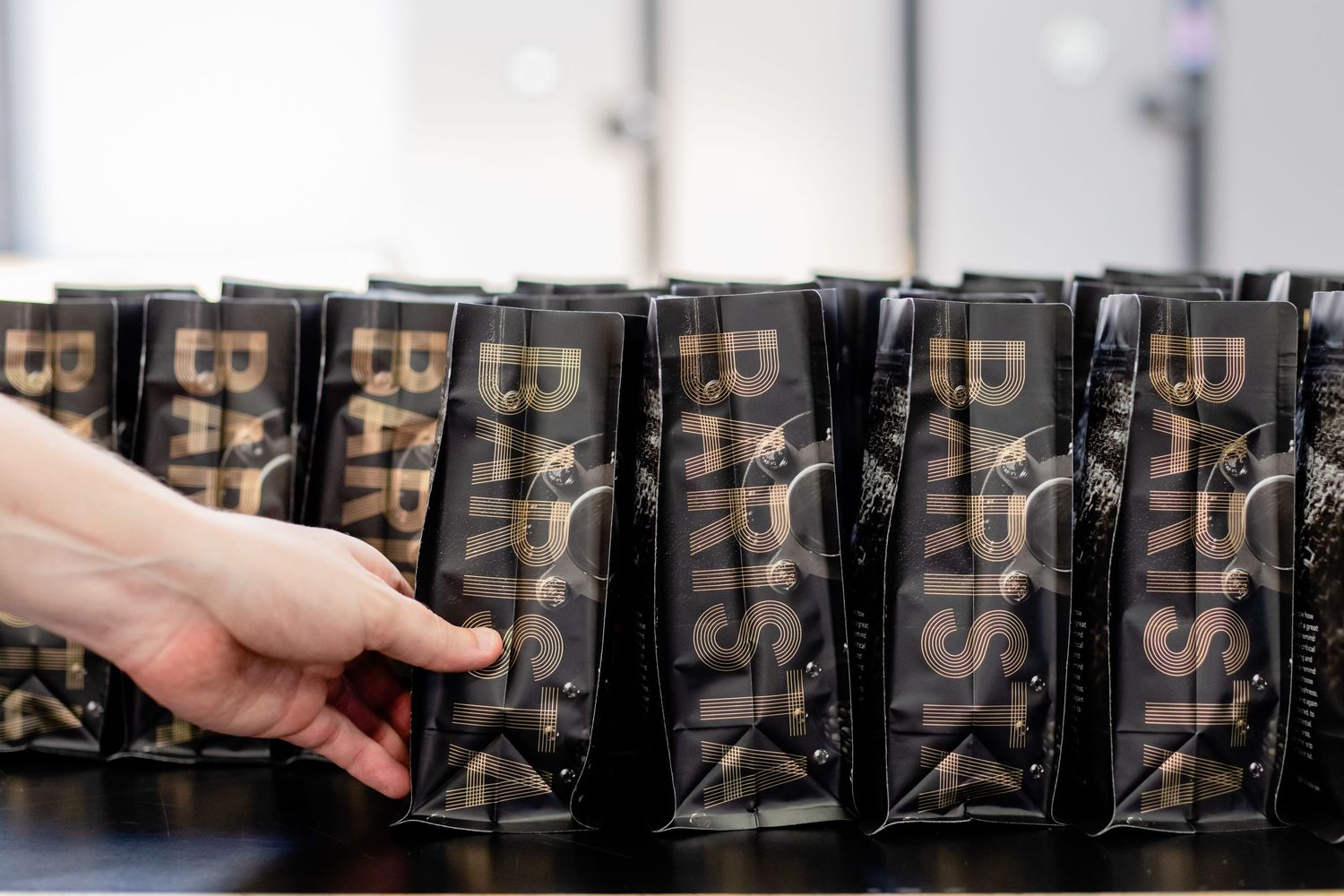 A hand reaches for black coffee bags with bold typography stacked on retail shelving.