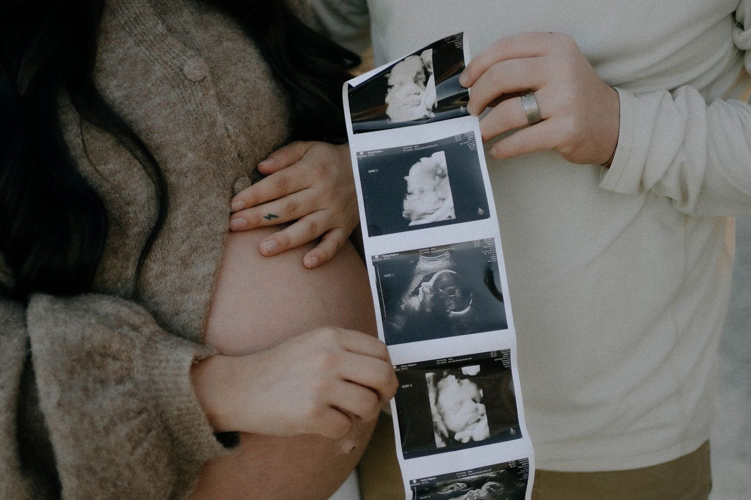 Close-up view of hands holding black and white ultrasound scan photos against a gray background.