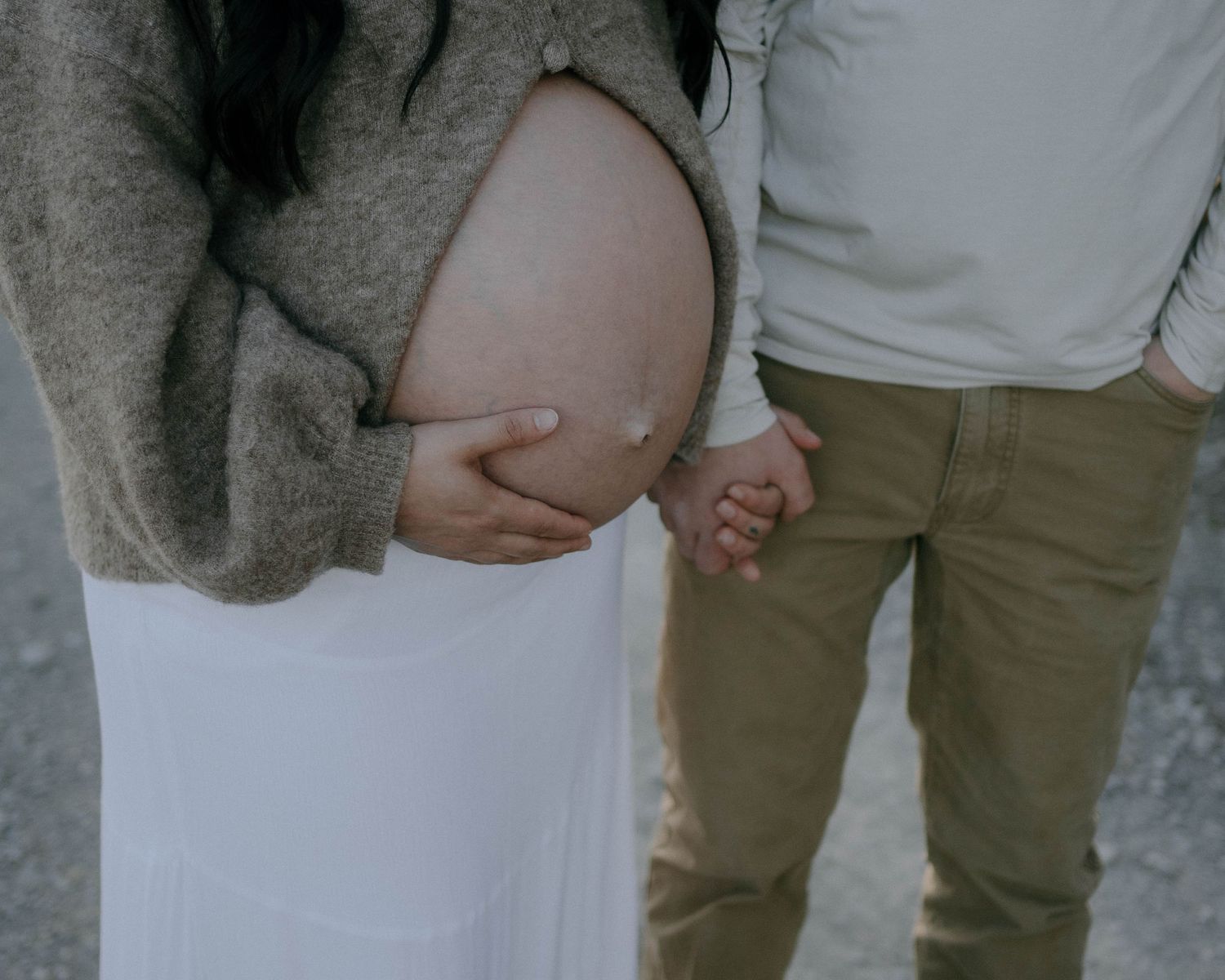 Close-up photo of expecting parents holding hands while gently touching a pregnant belly.