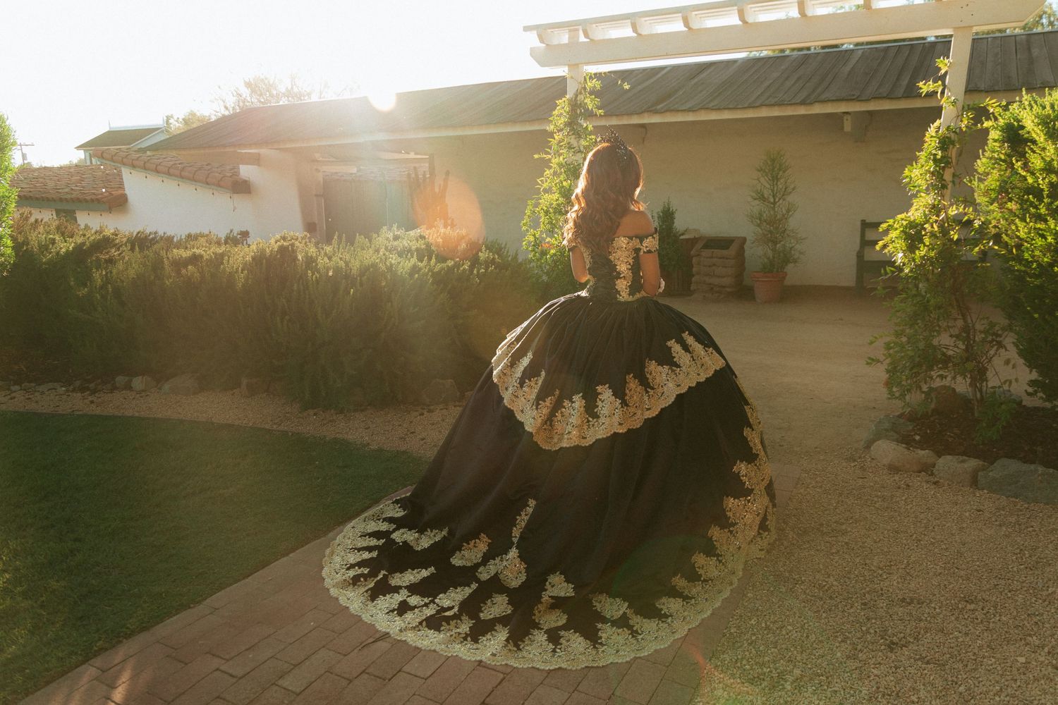 A silhouetted figure in an ornate dress stands in a backlit garden during golden hour creating a dramatic effect.