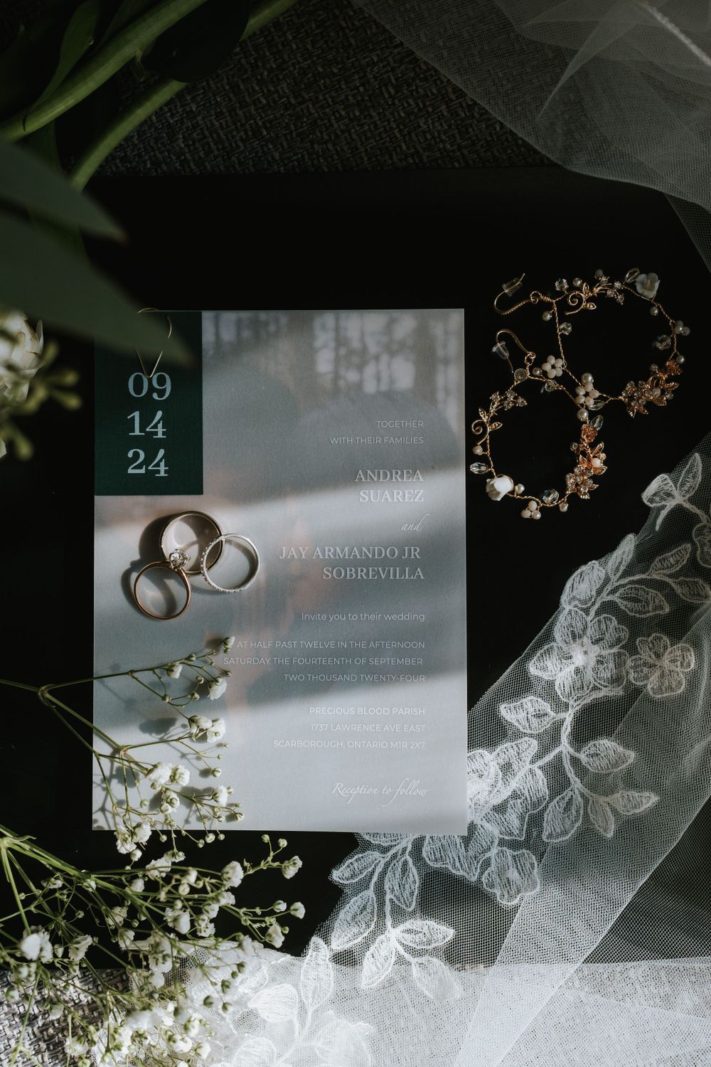 Wedding invitation with rings and delicate lace veil surrounded by baby's breath flowers and floral accessories.