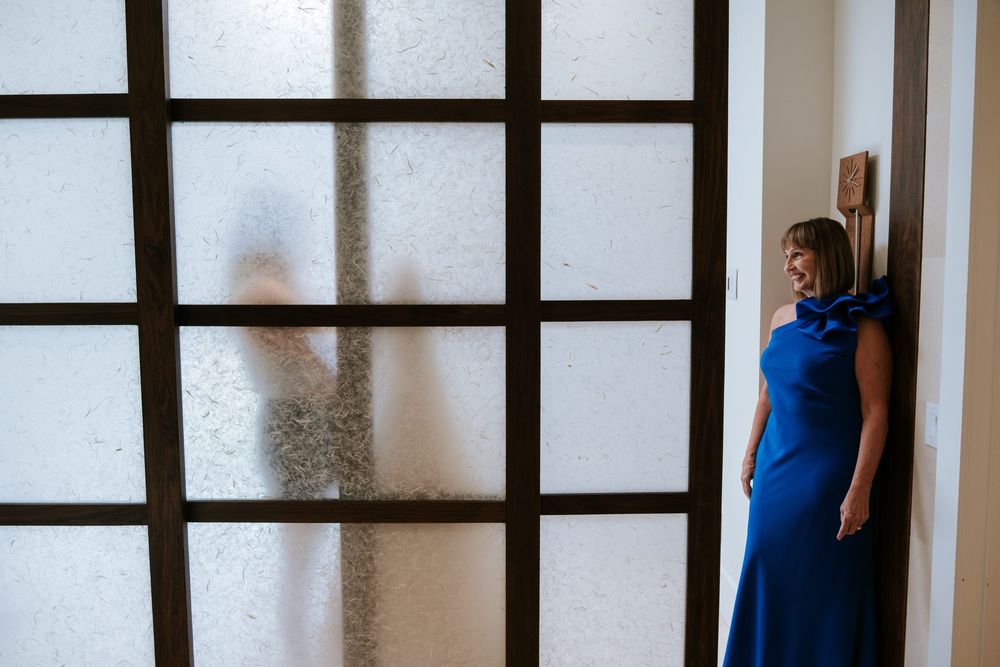 A person in a blue shirt stands near a dark-framed window in a white interior space.