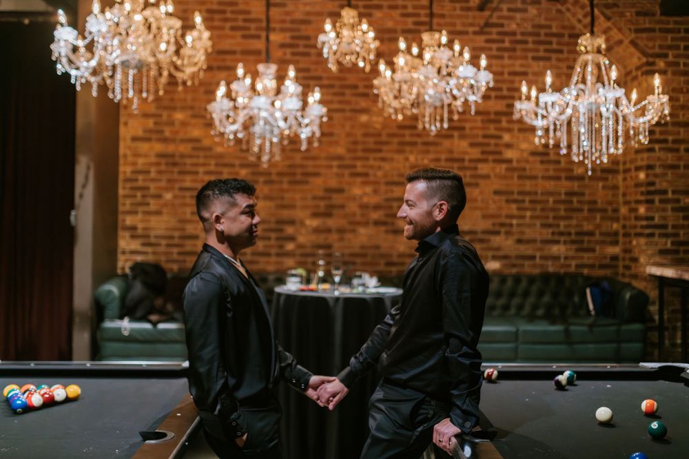 Elegant crystal chandeliers hang from exposed brick walls in a rustic-modern event venue space.