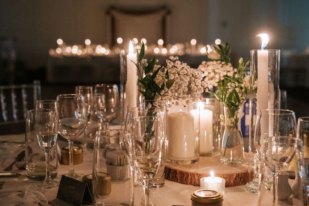 Elegant wedding reception tables decorated with glowing candles and crystal glassware in a romantic evening setting.