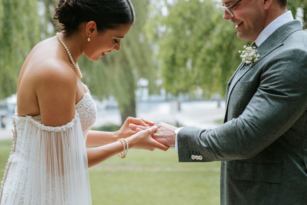 A couple shares an intimate moment during their wedding ceremony as they exchange rings in a garden setting.