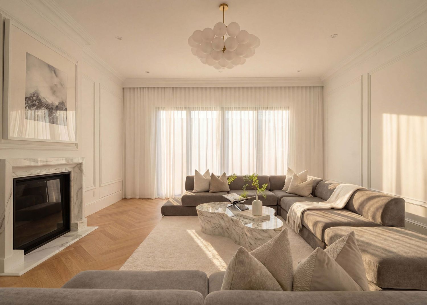 Modern living room with gray sectional sofa, herringbone wood floors, fireplace and sheer white curtains in natural light.
