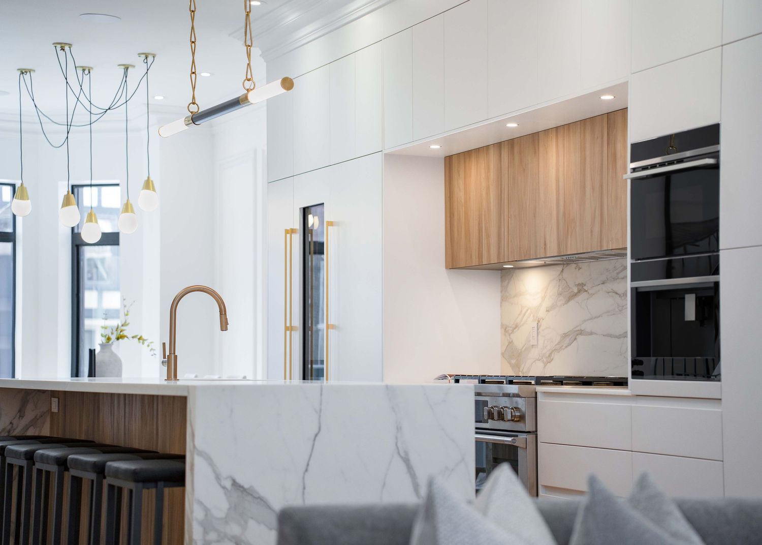 Modern kitchen interior with white marble backsplash, wooden cabinets, pendant lights and sleek stainless steel appliances.