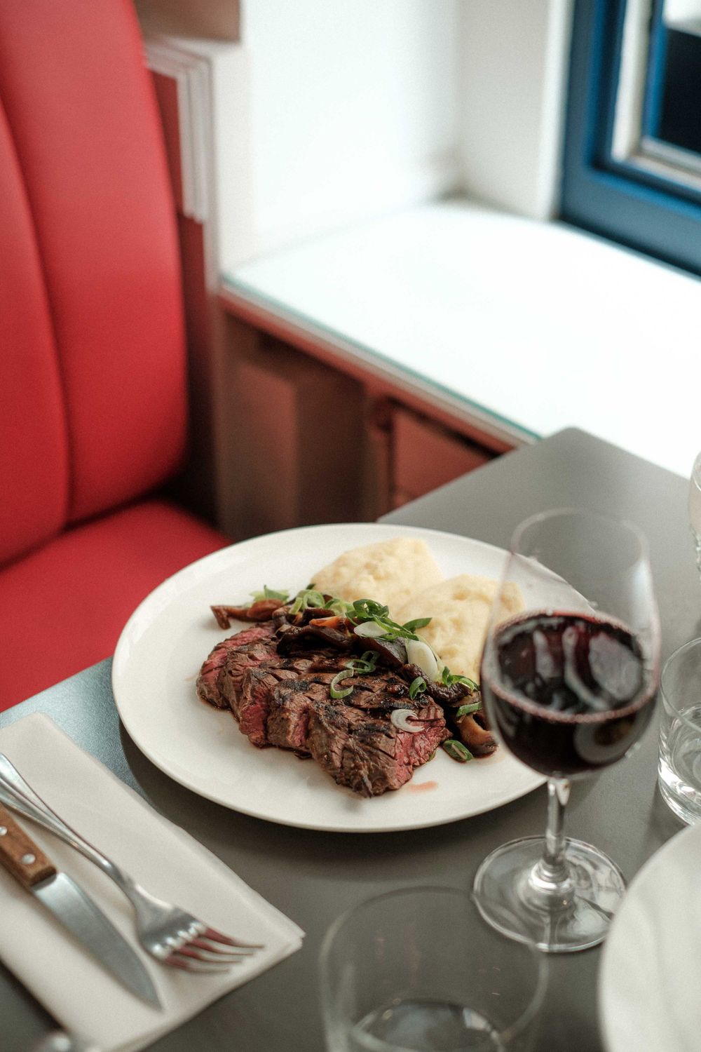 Grilled steak with mashed potatoes and red wine served on a white plate in an upscale setting.