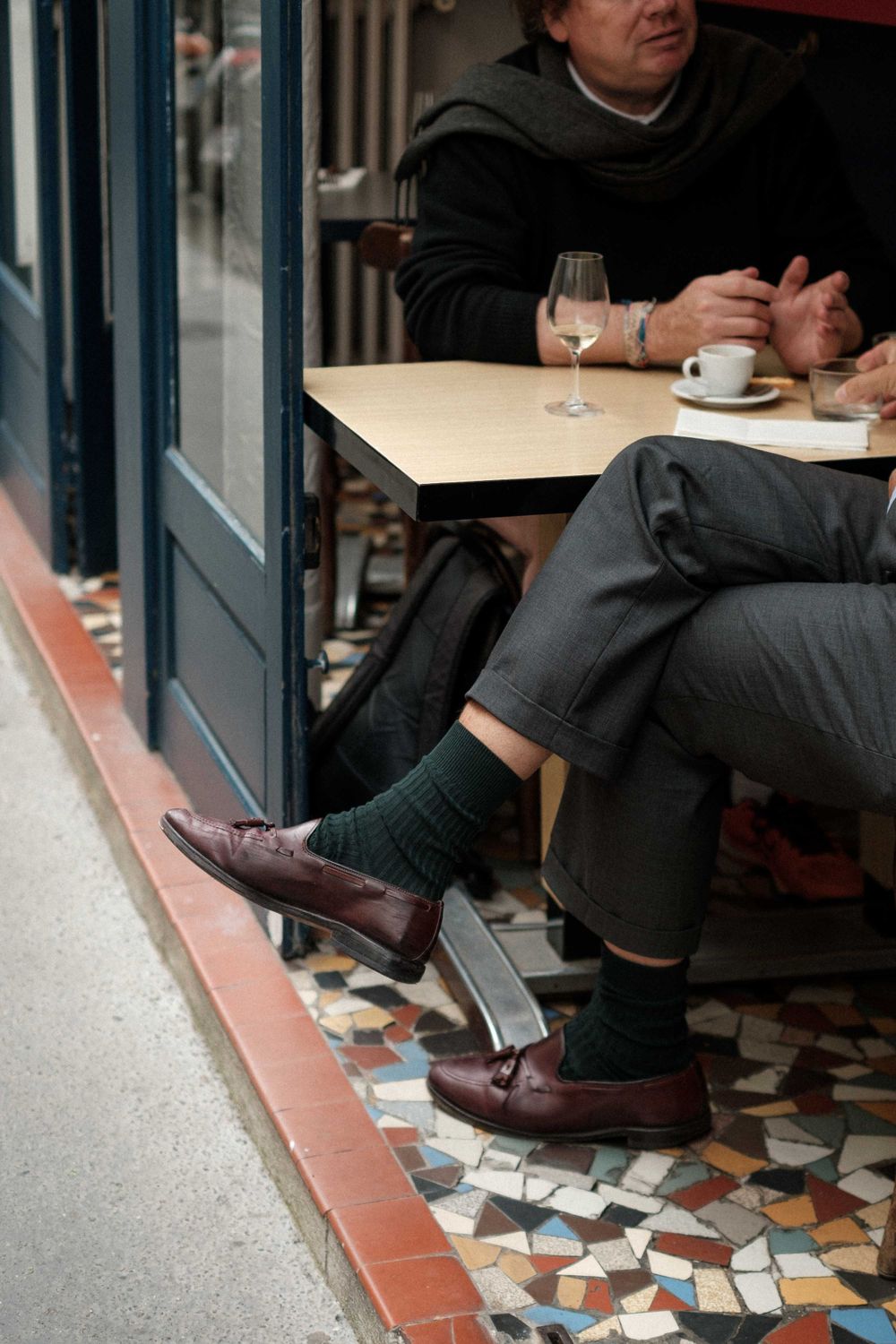 Brown leather shoes and dark socks on mosaic tile floor at outdoor cafe table.