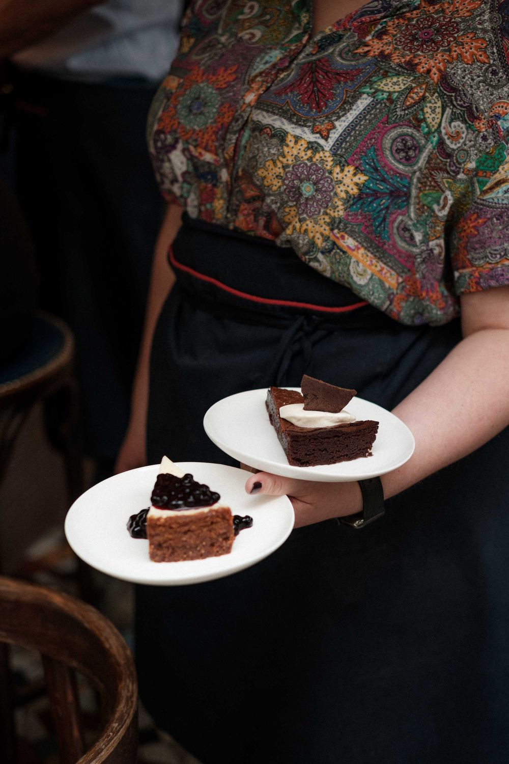 Server holding two plates of chocolate cake desserts with elegant plating.