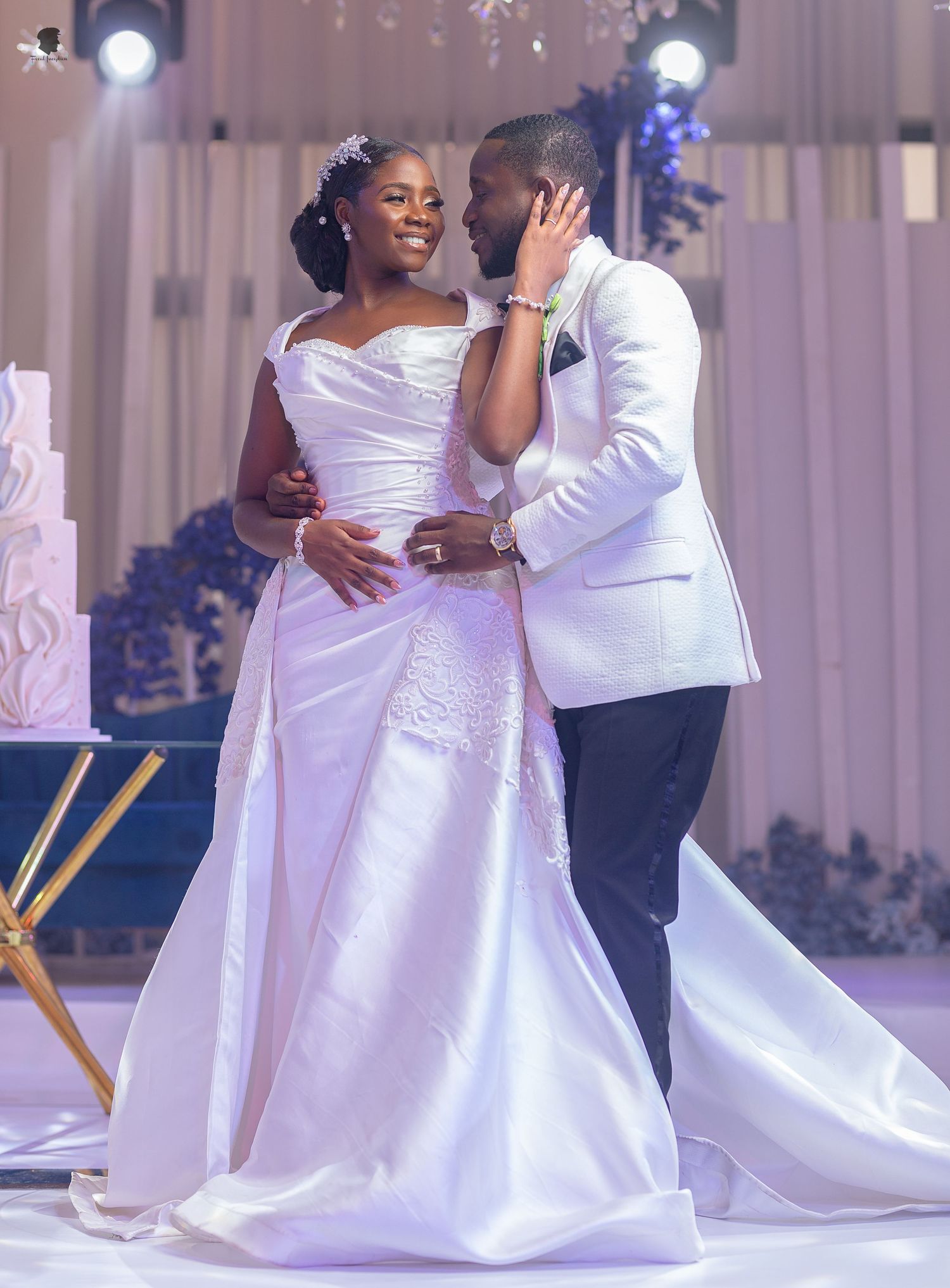Wedding couple share an intimate moment while dancing in their elegant white attire on the dance floor.