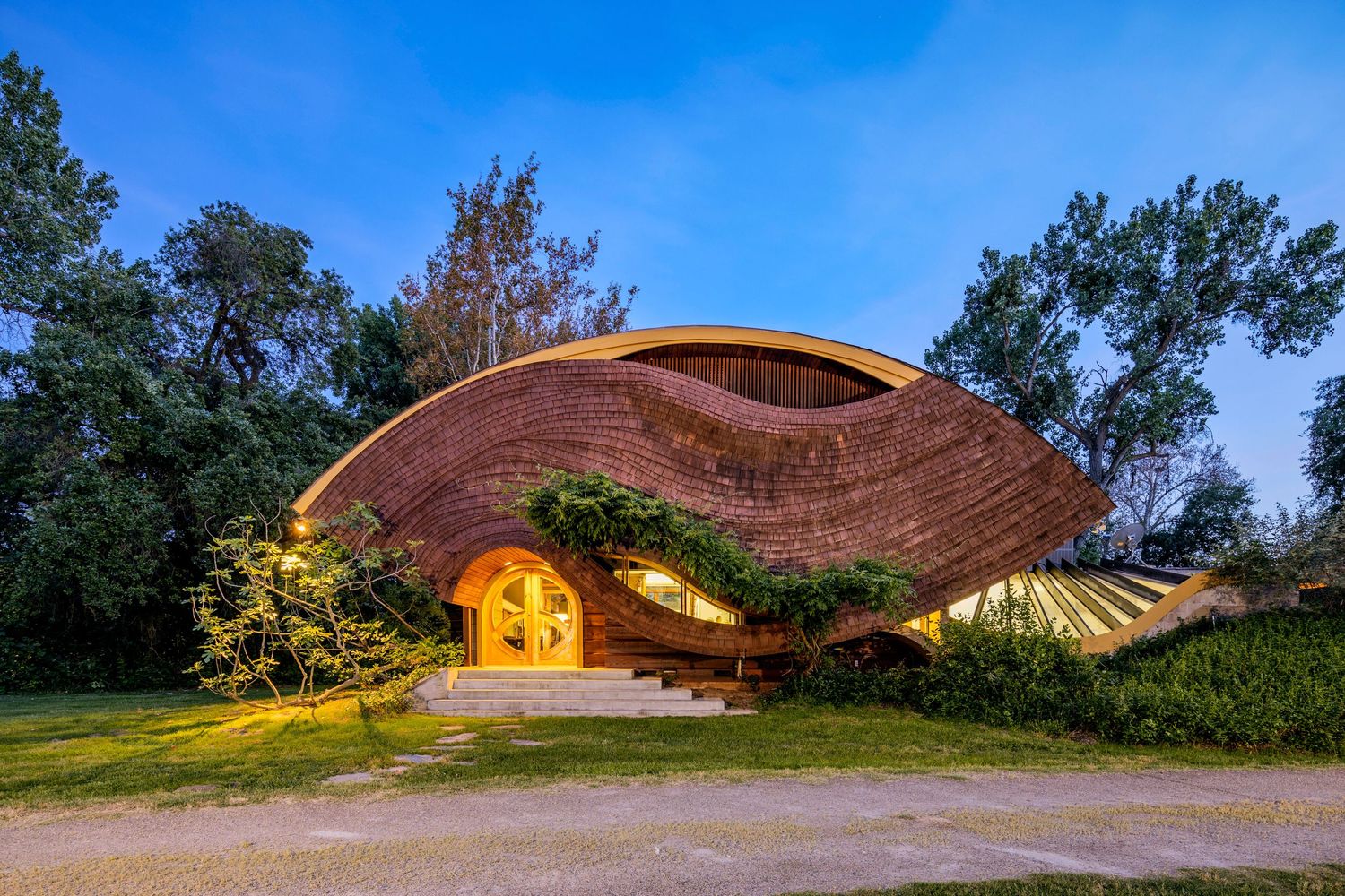 Unique curved wooden architecture with organic wave-like roof design illuminated at dusk. Arthur Dyson designed house.