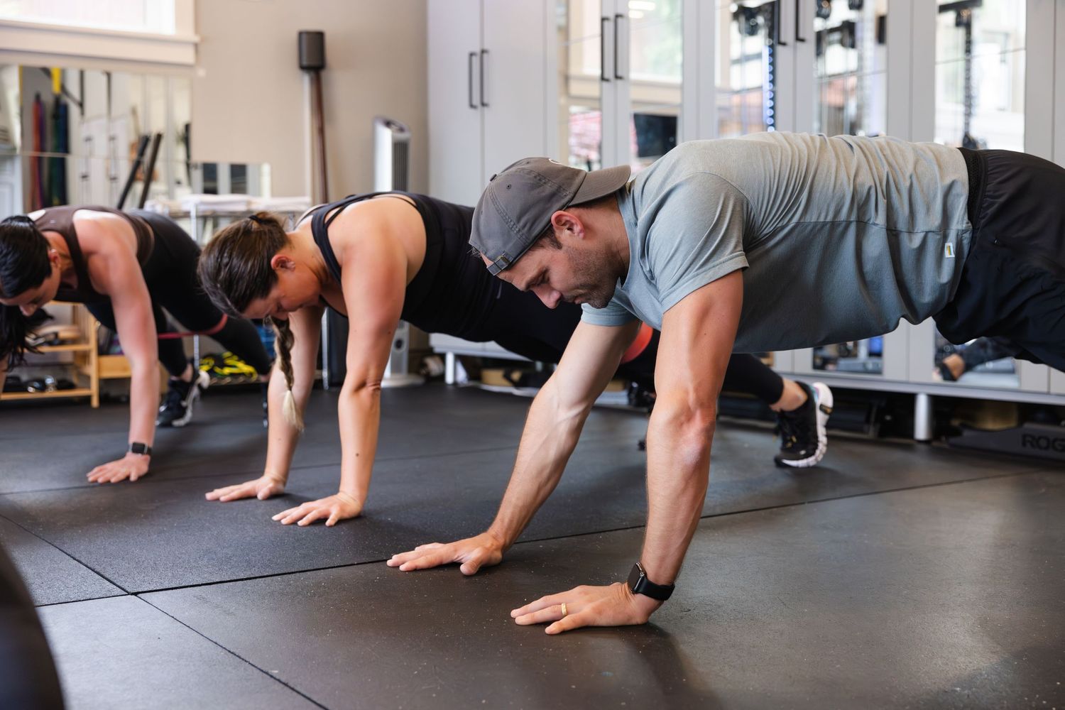 Group of people performing plank exercises on exercise mats in a modern fitness gym.
