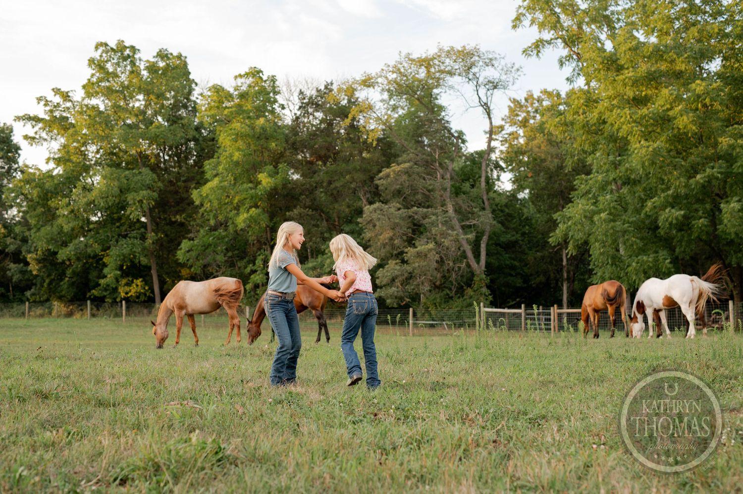 People standing in a pastoral field with horses grazing in the distant background during golden hour.