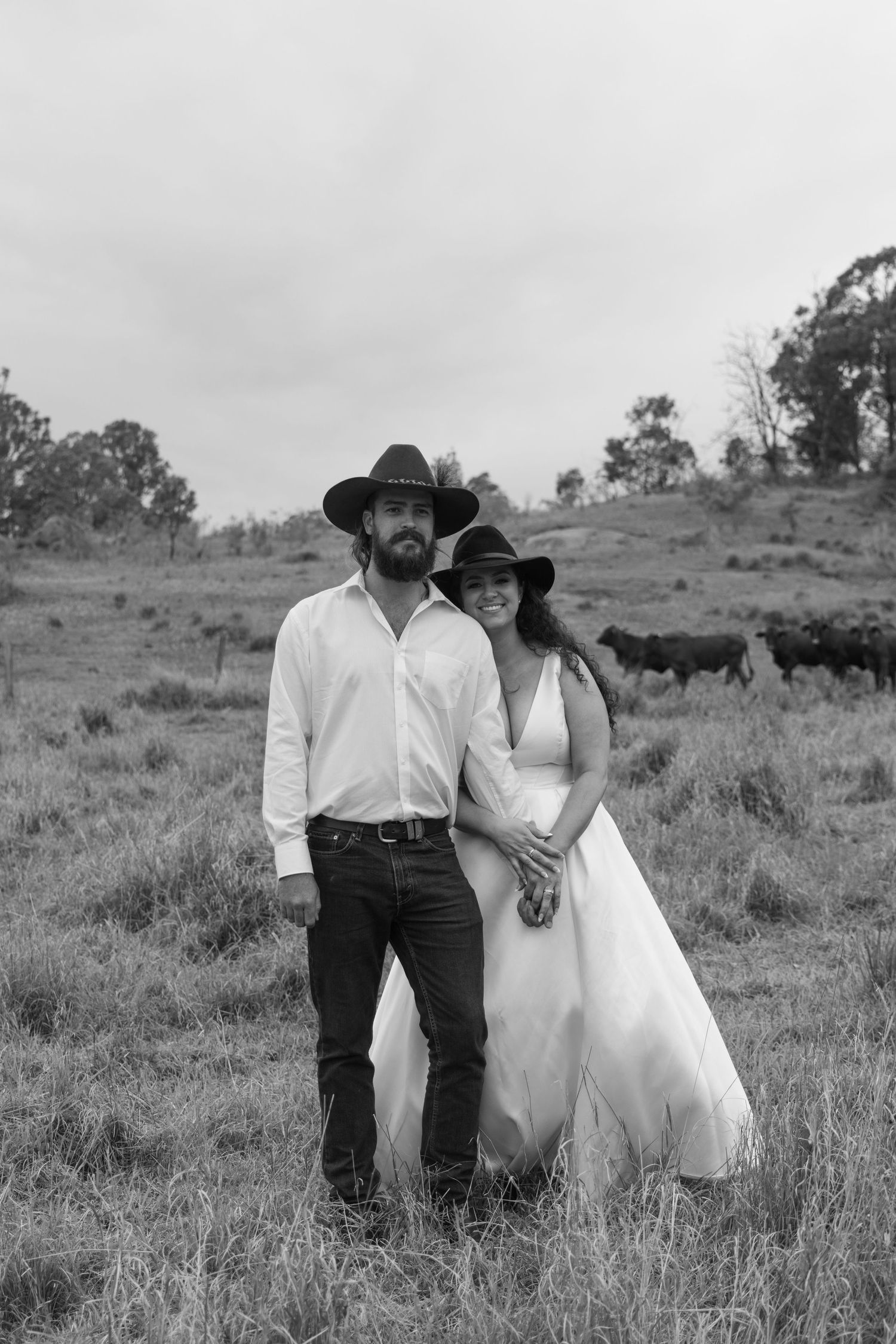 A romantic black and white portrait of a couple in wedding attire standing in a rural field.