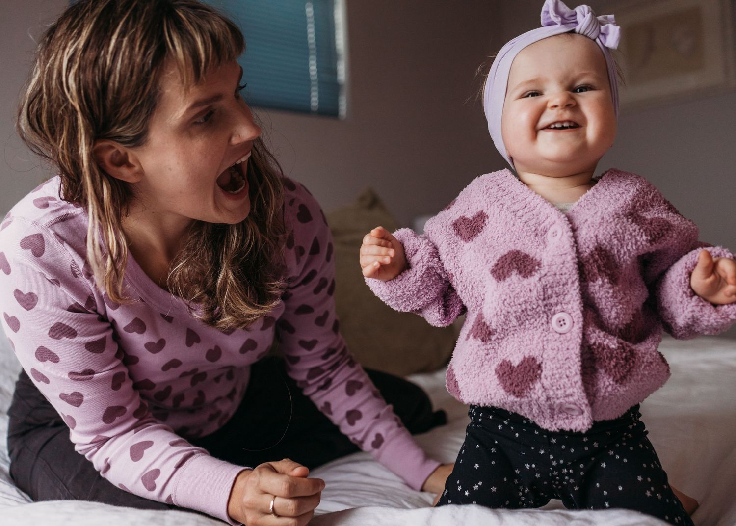 Two people in pink heart patterned sweaters share a playful moment together on the floor.