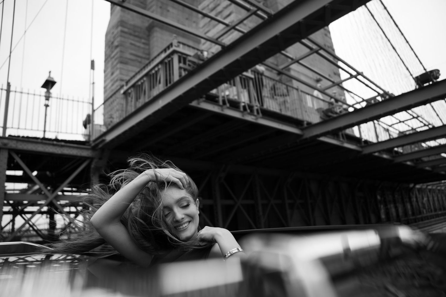 Black and white portrait under an industrial bridge or railway structure with shadows and architectural details.