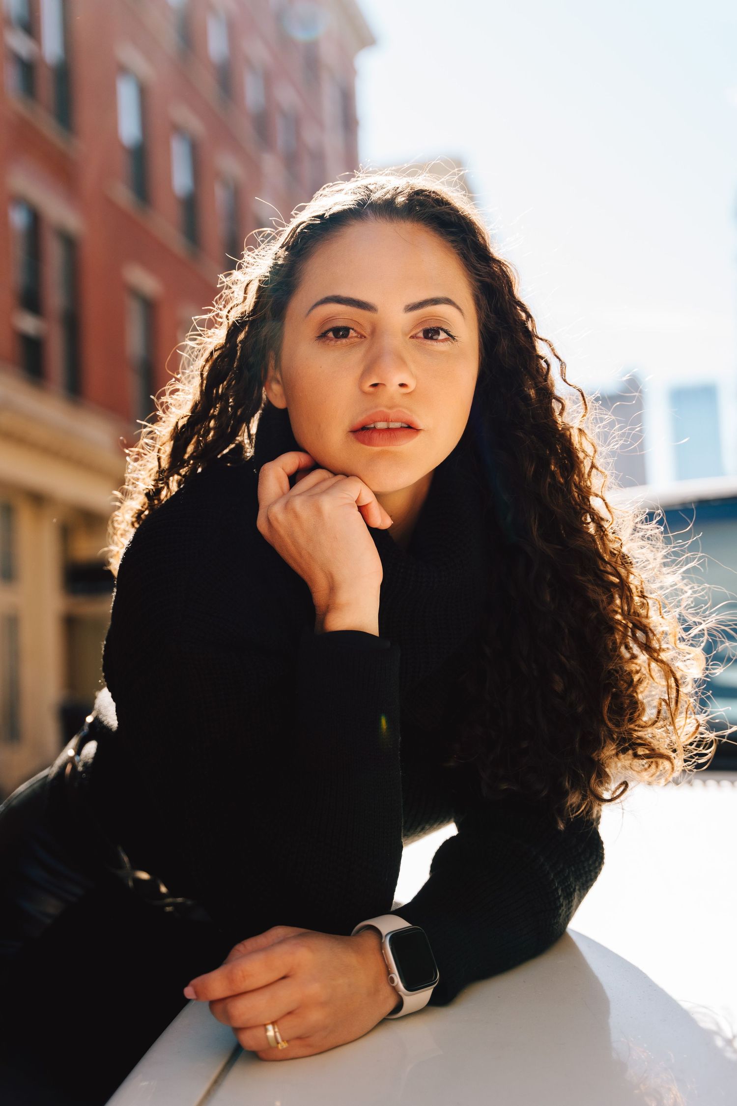 Person in black sweater poses against urban brick building backdrop.
