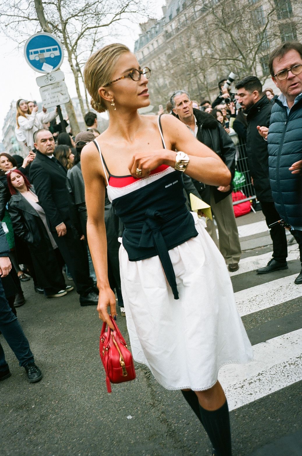 A fashionable street style look featuring a black and white dress with knee socks and a red handbag during Paris Fashion Week.