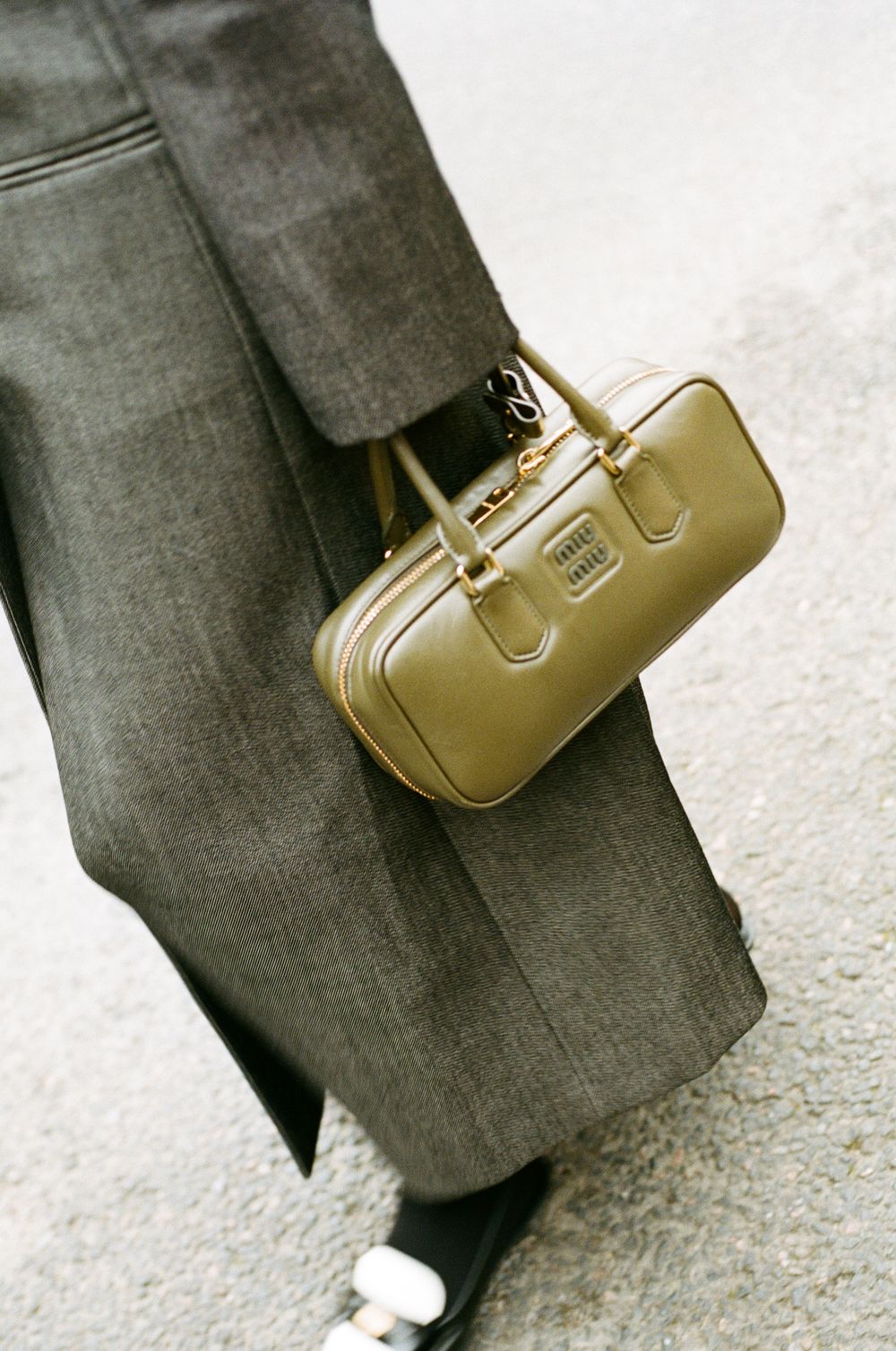Vintage gold leather handbag held against gray trousers and white sneakers in a minimalist fashion shot.