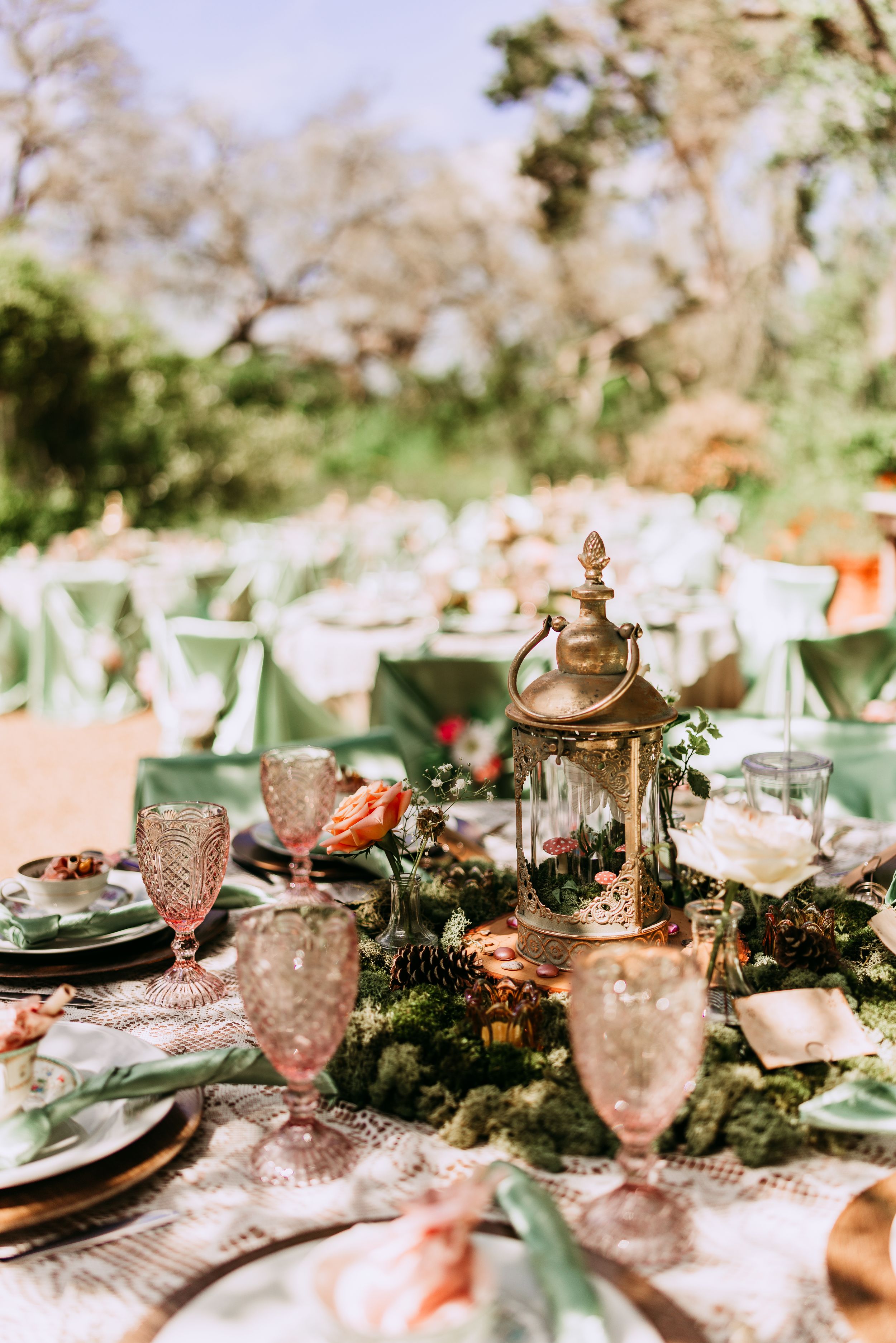 Elegant table setting with vintage glassware, greenery garland centerpiece, and antique brass decor in natural light.