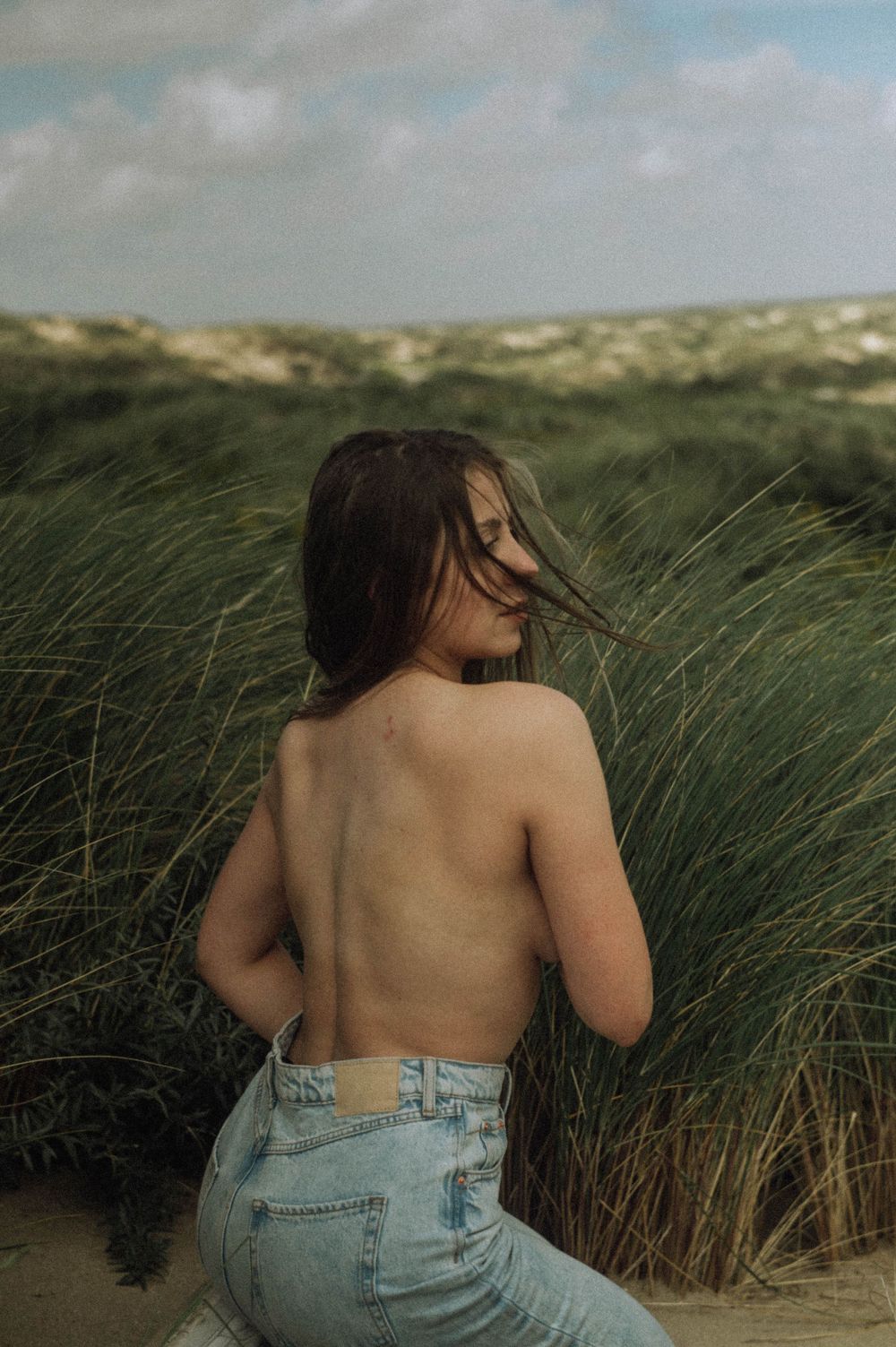 Artistic beach portrait showing denim and natural grasses against cloudy skies.