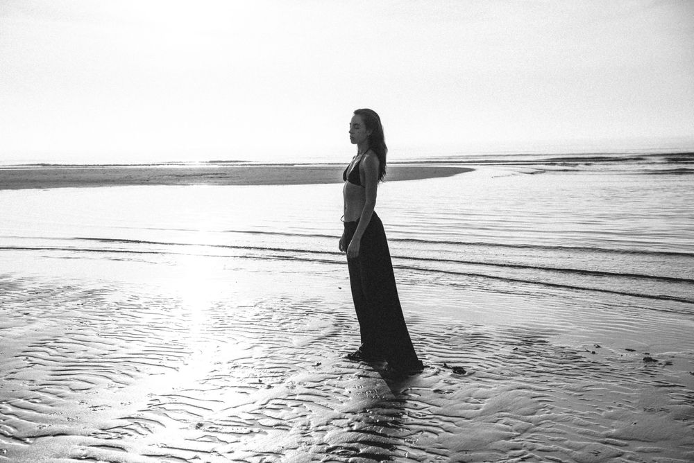 Silhouetted figure stands in shallow ocean water at sunset creating a dramatic coastal scene.