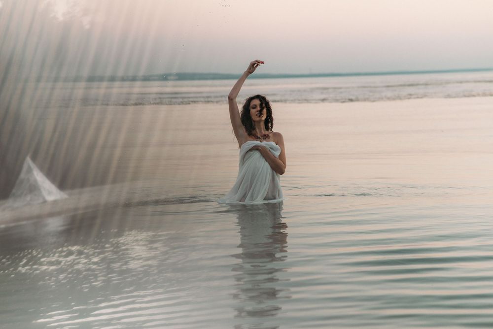 A person wades through calm ocean waters during sunset.