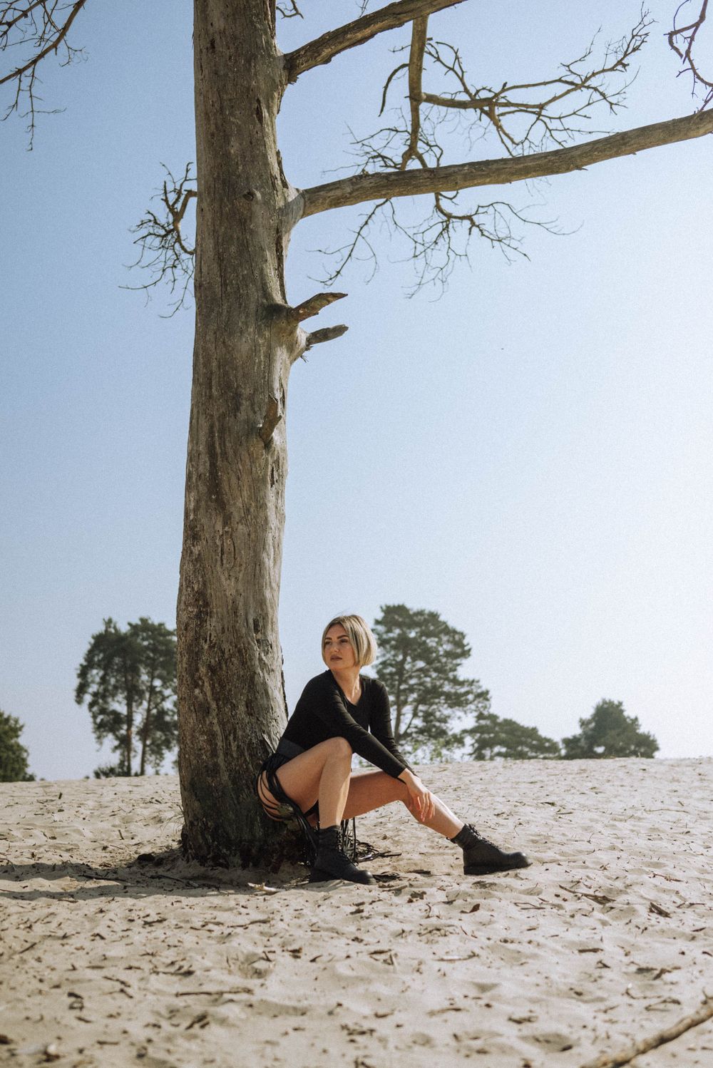 A person reclines against a large tree trunk on a sandy slope.