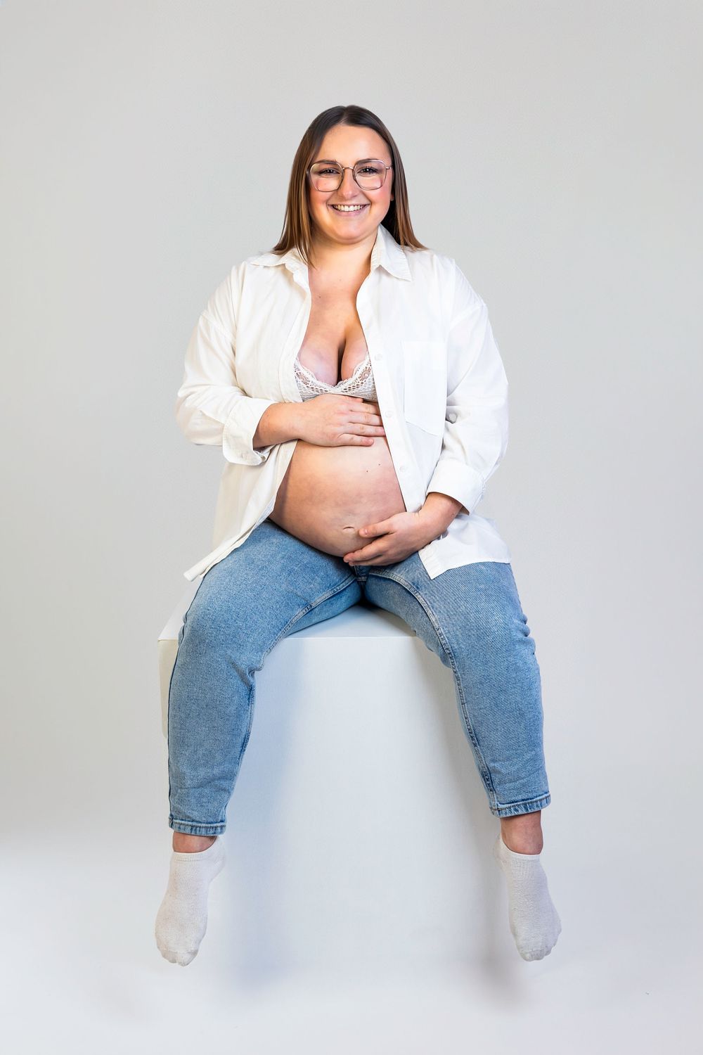 Séance photo minimaliste en studio d'une femme enceinte, capturant la douceur et la sérénité de la grossesse dans un cadre simple et épuré.