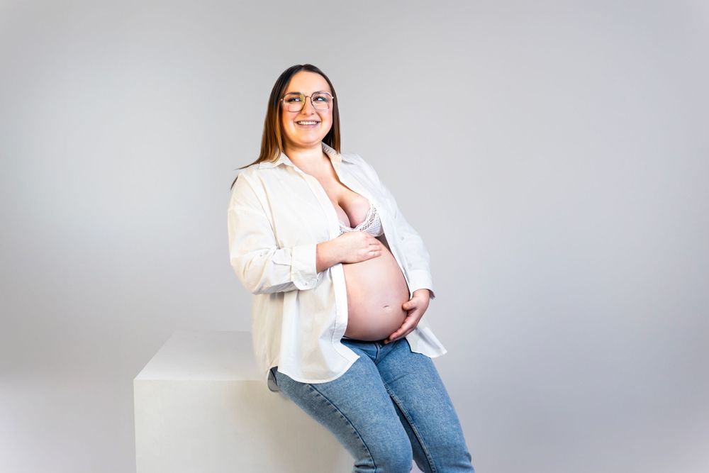 Séance photo minimaliste en studio d'une femme enceinte, capturant la douceur et la sérénité de la grossesse dans un cadre simple et épuré.