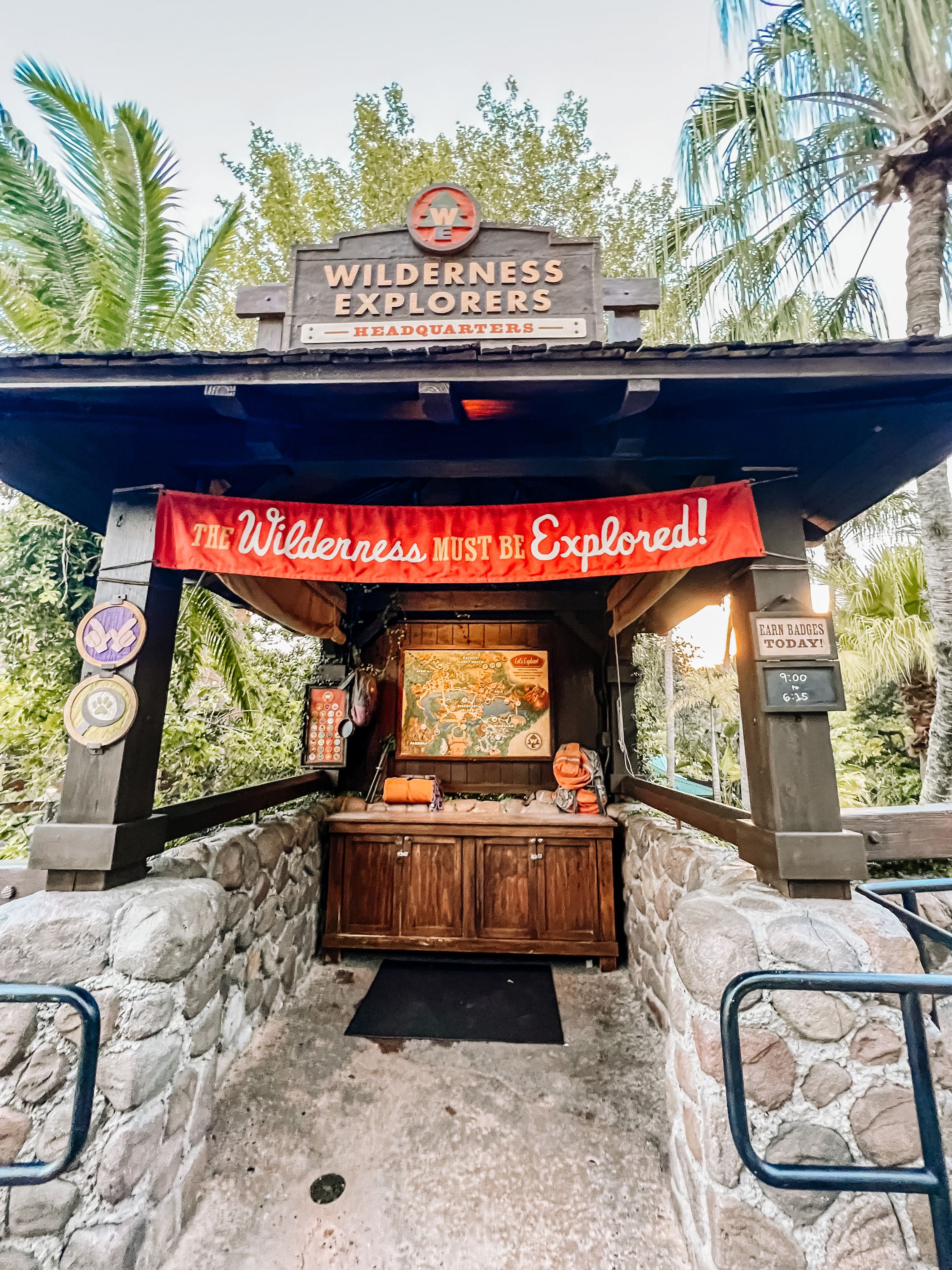 Wilderness Explorers kiosk with wooden booth and stone base under palm trees at Disney's Animal Kingdom theme park.