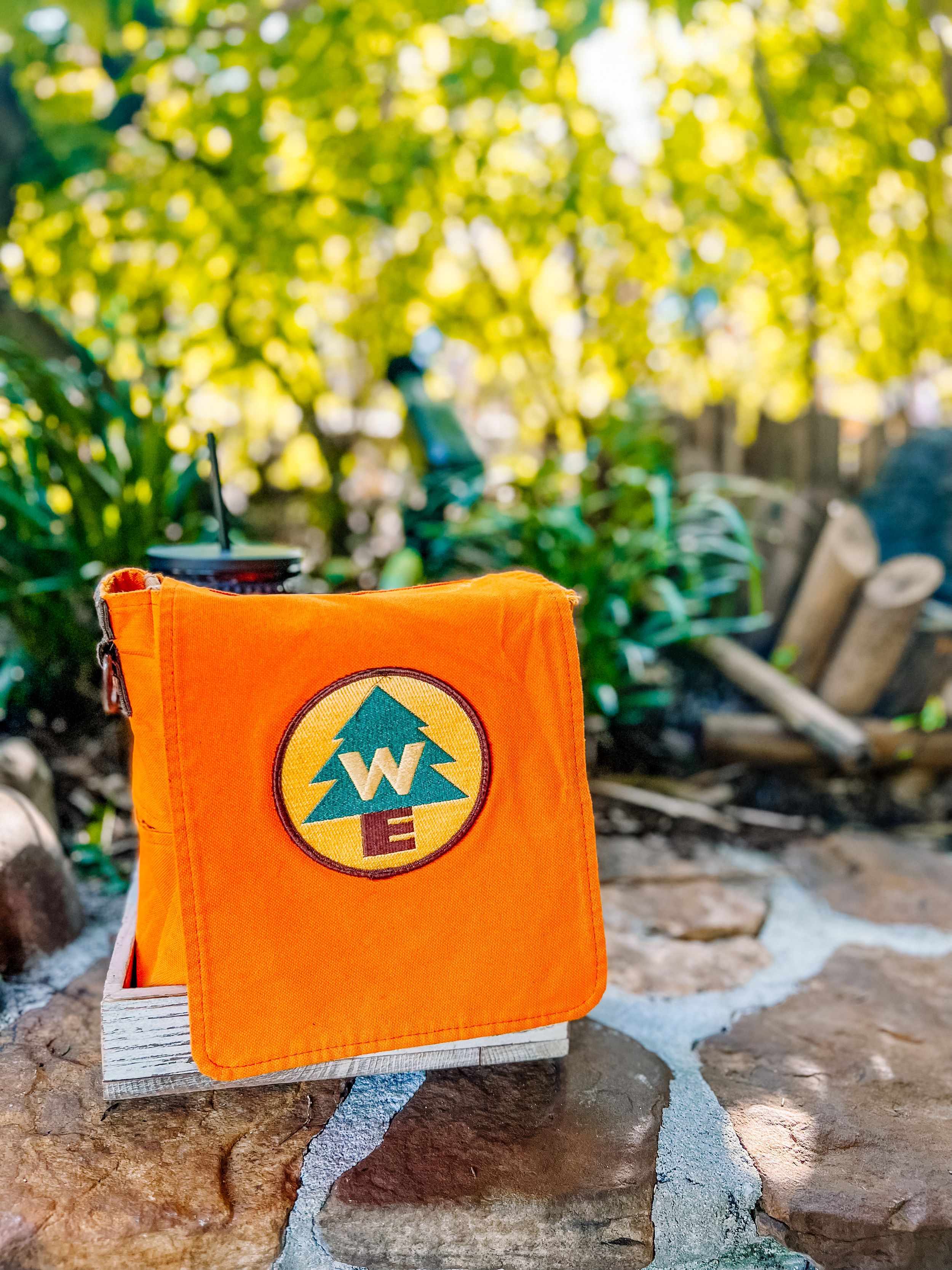 Orange leather wallet with embossed compass design displayed on natural stone surface in outdoor garden setting.
