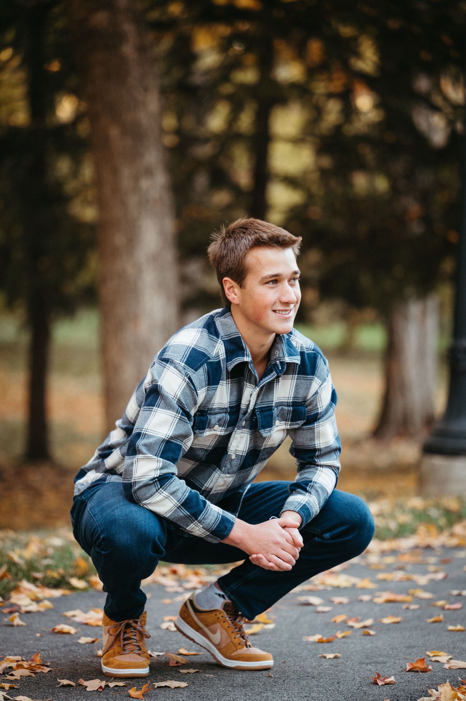 A casual portrait of someone crouching in a plaid flannel shirt against an autumn backdrop.