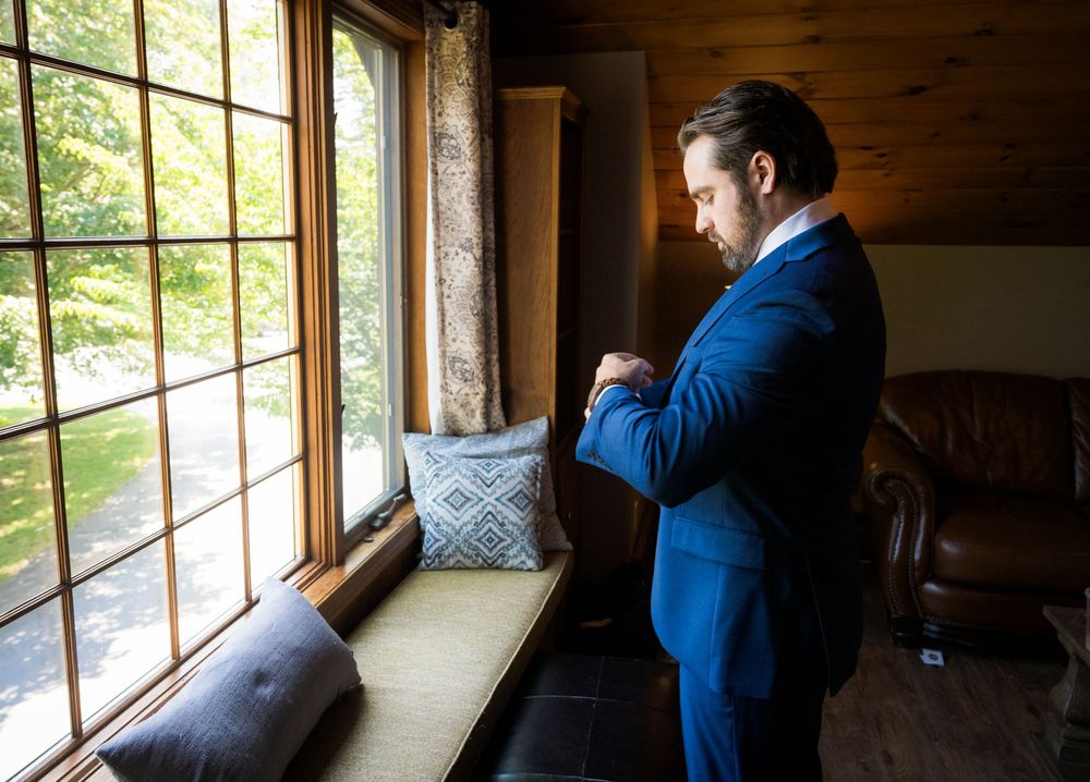People in blue suits looking through windows in a rustic wooden room during a wedding preparation.