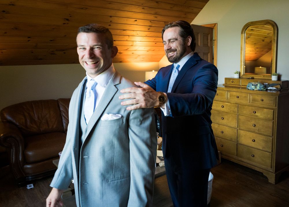 Groomsmen get ready in a rustic wood-paneled room wearing light blue suits and navy ties.