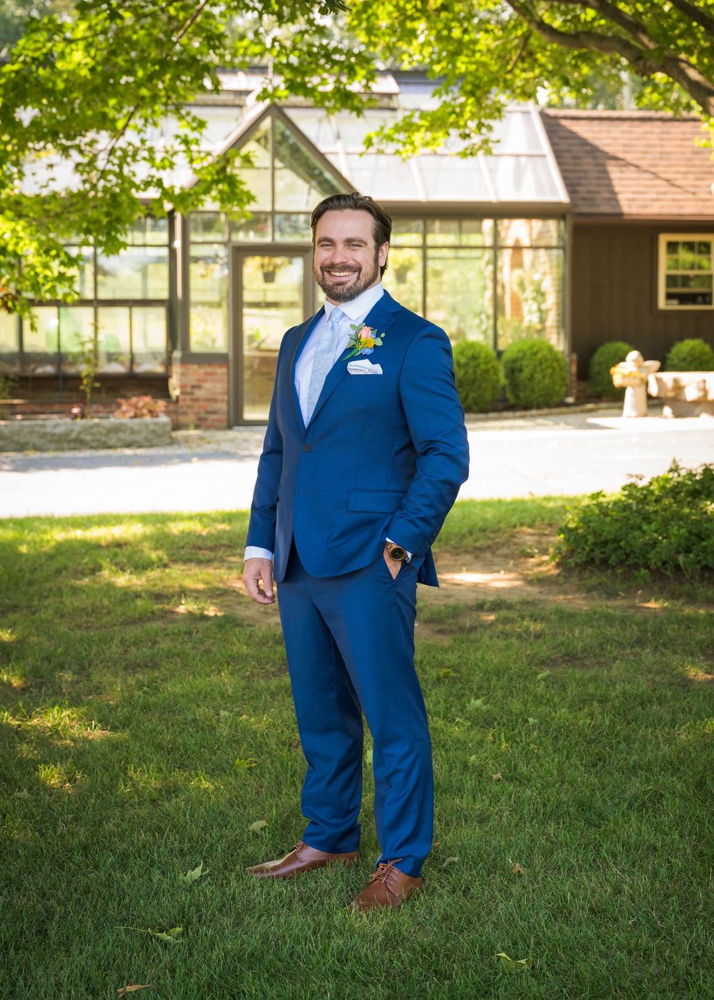 Groomsmen in navy blue suits posing on a sunny lawn with trees in background.